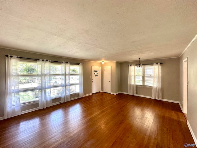 empty room featuring a textured ceiling, ornamental molding, a chandelier, and dark hardwood / wood-style flooring