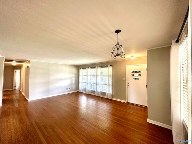 spare room featuring crown molding, a textured ceiling, a notable chandelier, and dark hardwood / wood-style floors