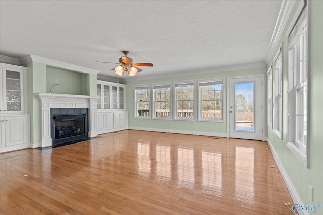 interior space with light hardwood / wood-style floors, a textured ceiling, a tile fireplace, ornamental molding, and ceiling fan