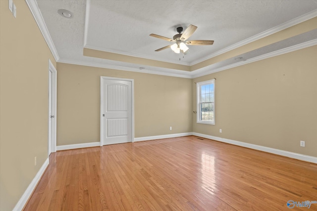 spare room featuring light wood-type flooring, ornamental molding, a textured ceiling, and a tray ceiling