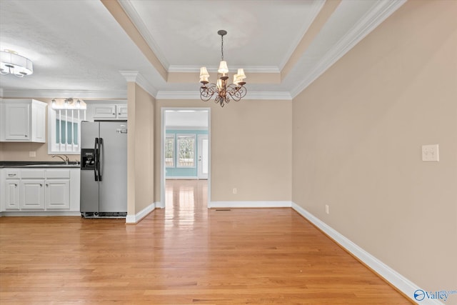 unfurnished dining area with crown molding, light hardwood / wood-style floors, a chandelier, sink, and a tray ceiling