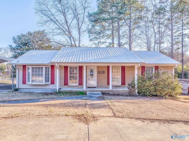 ranch-style home featuring covered porch, brick siding, and metal roof