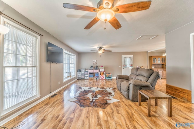 living area featuring visible vents, baseboards, a ceiling fan, a textured ceiling, and light wood-style floors