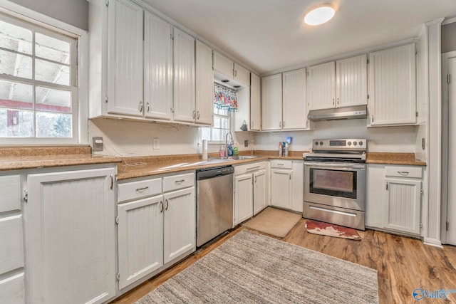 kitchen with white cabinets, stainless steel appliances, light countertops, under cabinet range hood, and a sink