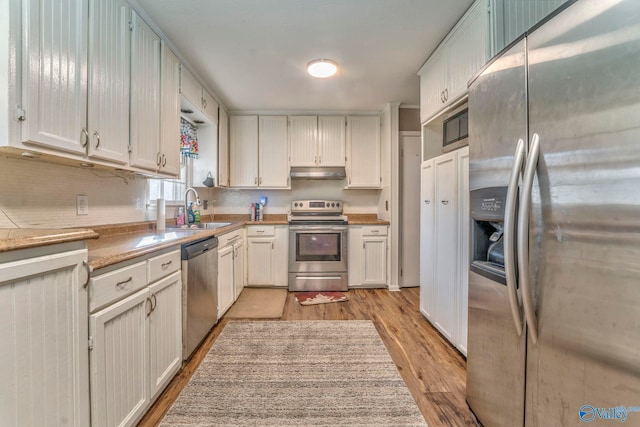 kitchen with light countertops, appliances with stainless steel finishes, white cabinetry, light wood-type flooring, and under cabinet range hood