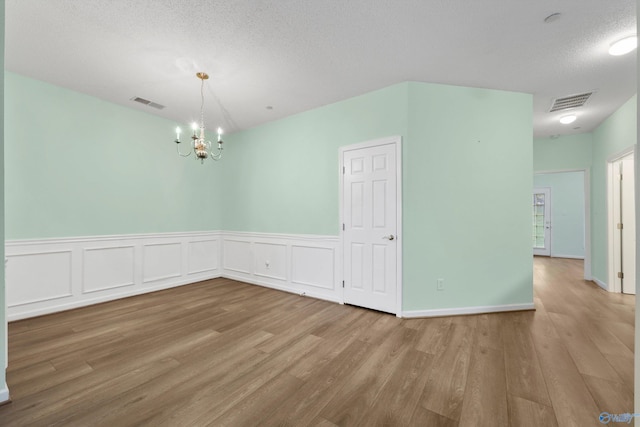 spare room with wood-type flooring, a textured ceiling, and a notable chandelier