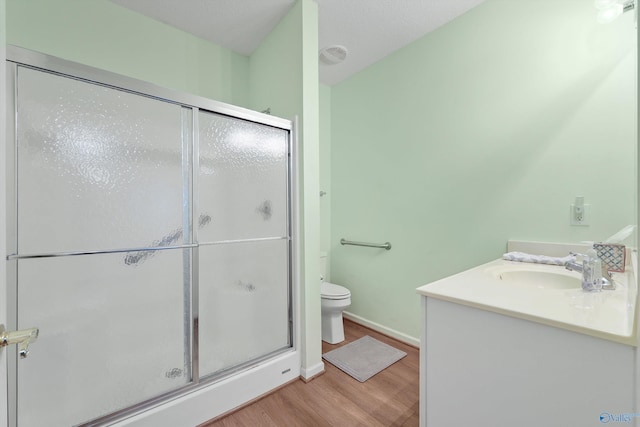 bathroom featuring vanity, toilet, a shower with shower door, and wood-type flooring