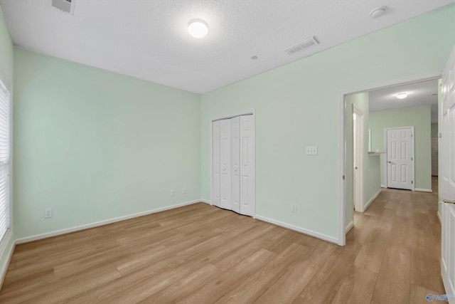 unfurnished bedroom with a textured ceiling, light hardwood / wood-style floors, and a closet