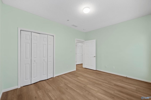 unfurnished bedroom featuring a textured ceiling, light wood-type flooring, and a closet