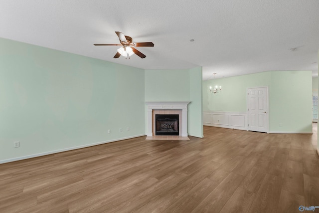 unfurnished living room featuring a textured ceiling, ceiling fan with notable chandelier, light hardwood / wood-style floors, and a tiled fireplace