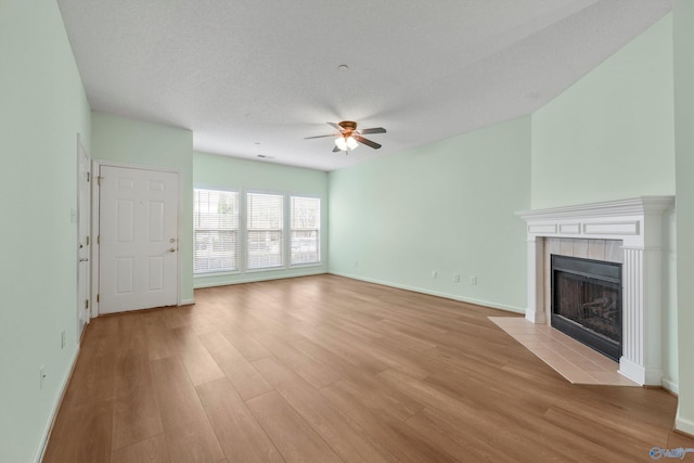 unfurnished living room with ceiling fan, light wood-type flooring, a textured ceiling, and a tile fireplace