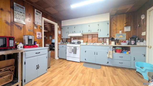 kitchen with light hardwood / wood-style floors, wood walls, white gas range, and sink