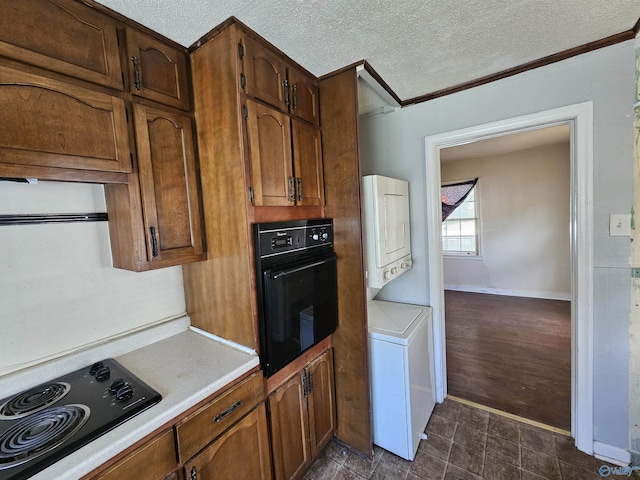 kitchen with a textured ceiling, stacked washer / dryer, light countertops, baseboards, and black appliances