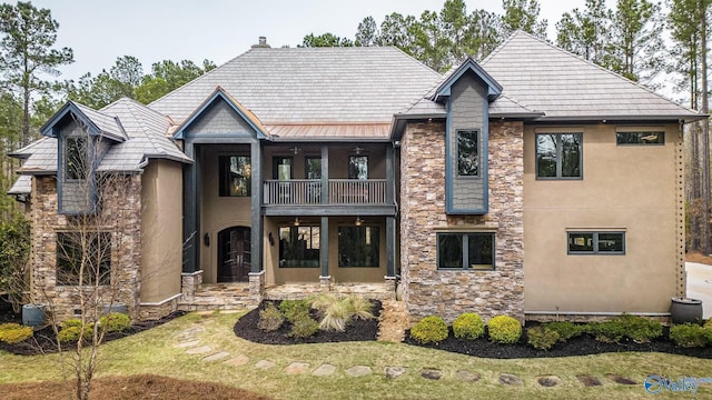 view of front of home featuring a balcony, stone siding, stucco siding, a standing seam roof, and a front yard