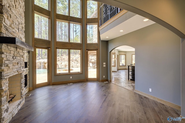 unfurnished living room featuring baseboards, arched walkways, a towering ceiling, wood finished floors, and a fireplace