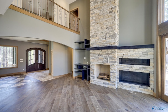 unfurnished living room featuring a stone fireplace, a towering ceiling, and hardwood / wood-style floors