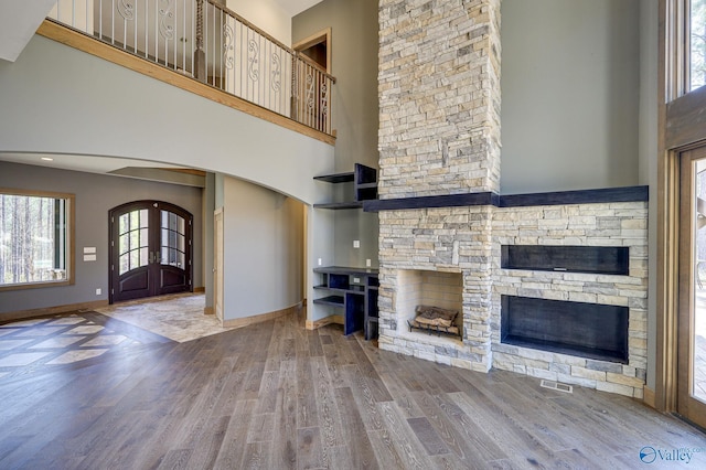 unfurnished living room featuring arched walkways, a stone fireplace, wood finished floors, baseboards, and french doors