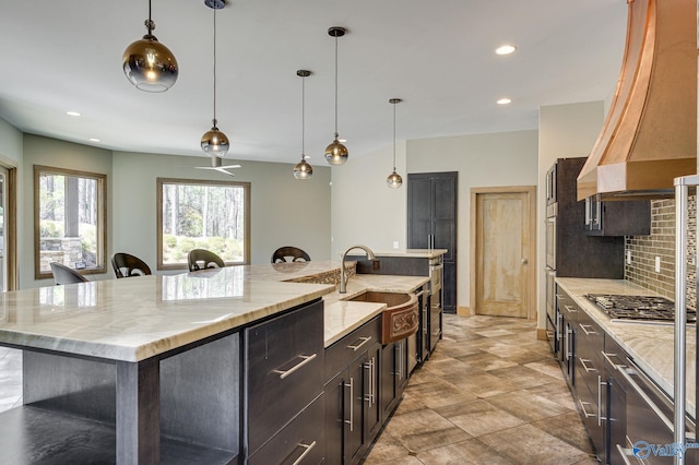 kitchen with custom range hood, stainless steel gas stovetop, light tile patterned floors, decorative backsplash, and a spacious island