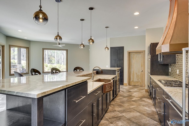kitchen featuring a large island, backsplash, premium range hood, stainless steel gas stovetop, and a sink