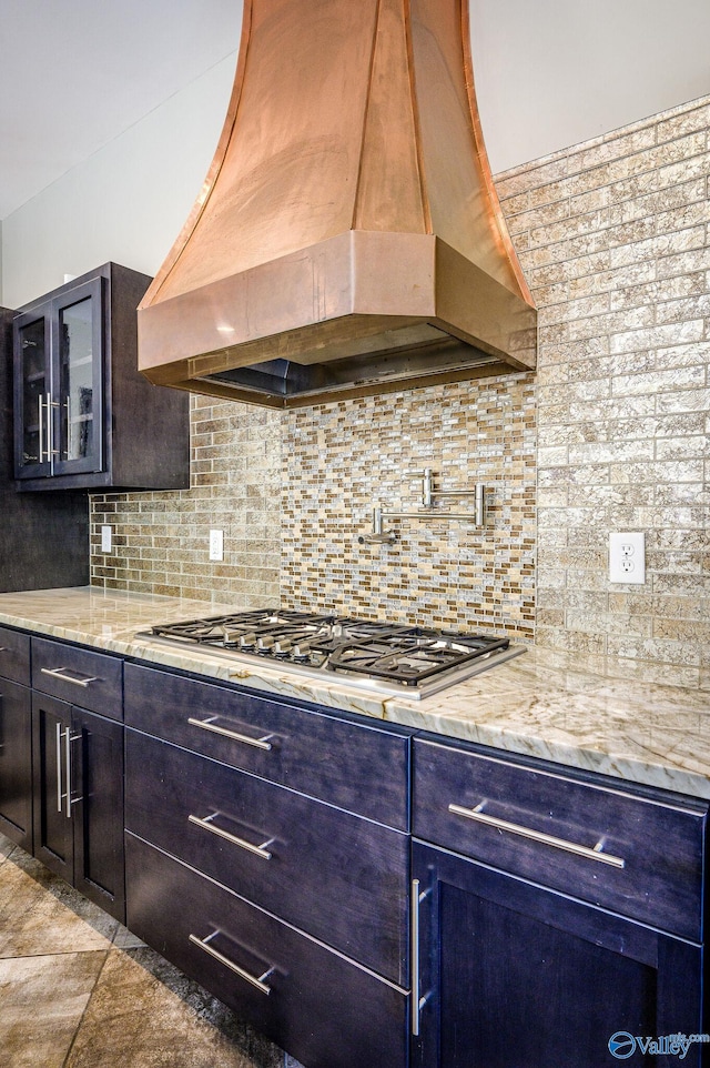 kitchen with stainless steel gas stovetop, light stone counters, premium range hood, light tile patterned floors, and decorative backsplash