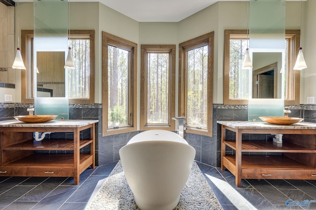 interior space with a soaking tub, two vanities, and tile walls