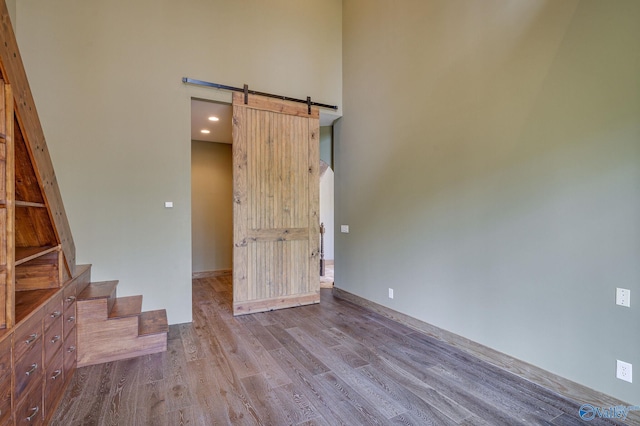 unfurnished room with stairs, a barn door, a towering ceiling, and wood finished floors