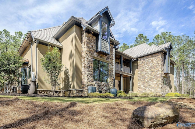 view of property exterior with stone siding, a balcony, and stucco siding