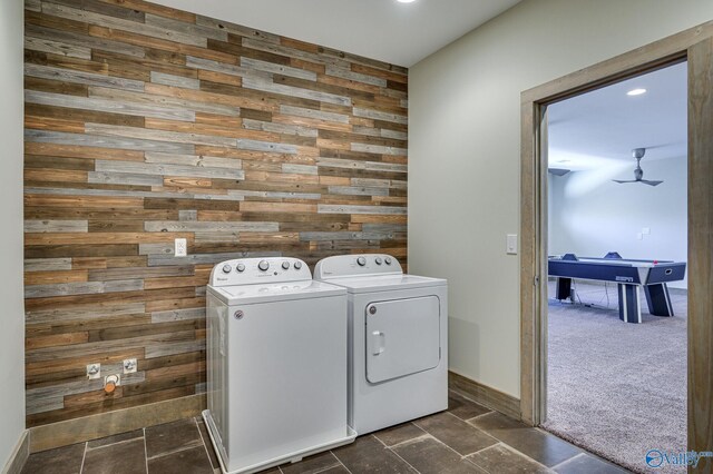washroom featuring wood walls, an accent wall, washer and clothes dryer, and stone tile flooring