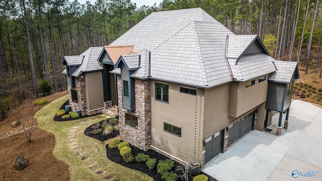 view of side of home with a garage, stone siding, concrete driveway, stucco siding, and a wooded view