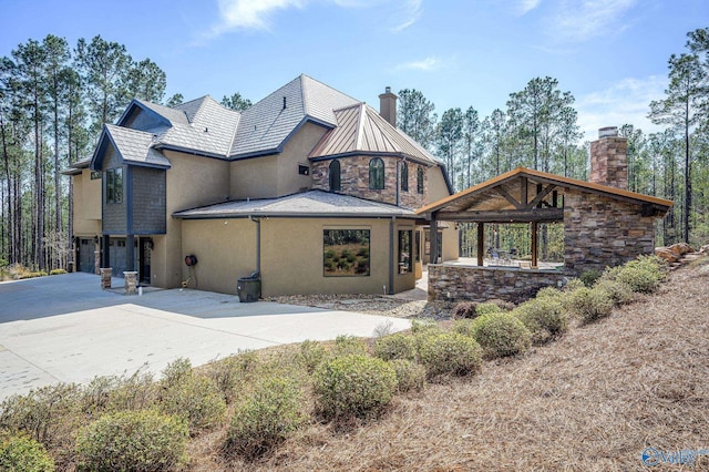 rear view of house with a standing seam roof, a garage, stone siding, driveway, and a chimney