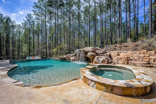 view of swimming pool featuring a patio, a pool with connected hot tub, and a view of trees