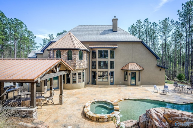 rear view of property featuring a chimney, a standing seam roof, a patio area, metal roof, and an in ground hot tub