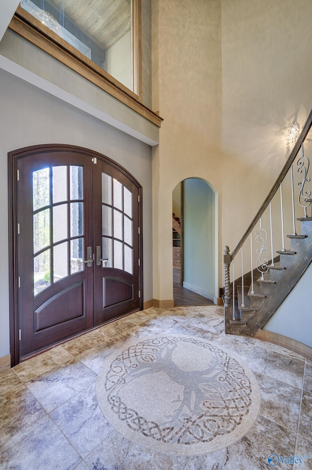 entrance foyer featuring baseboards, arched walkways, a towering ceiling, stairway, and french doors