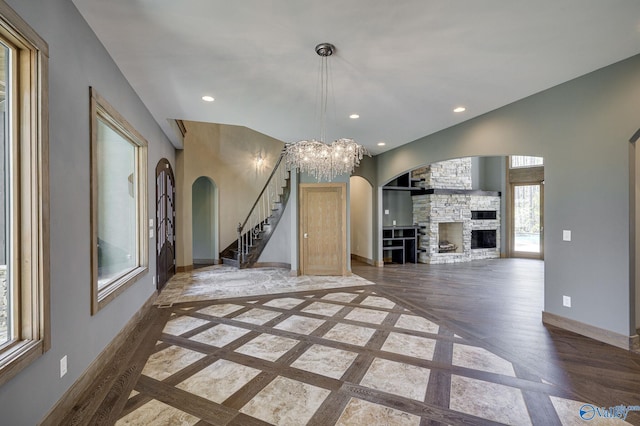 unfurnished living room featuring a stone fireplace, built in shelves, and a notable chandelier