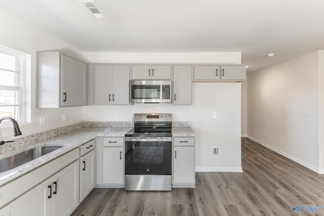 kitchen featuring sink, stainless steel appliances, light stone counters, and hardwood / wood-style floors