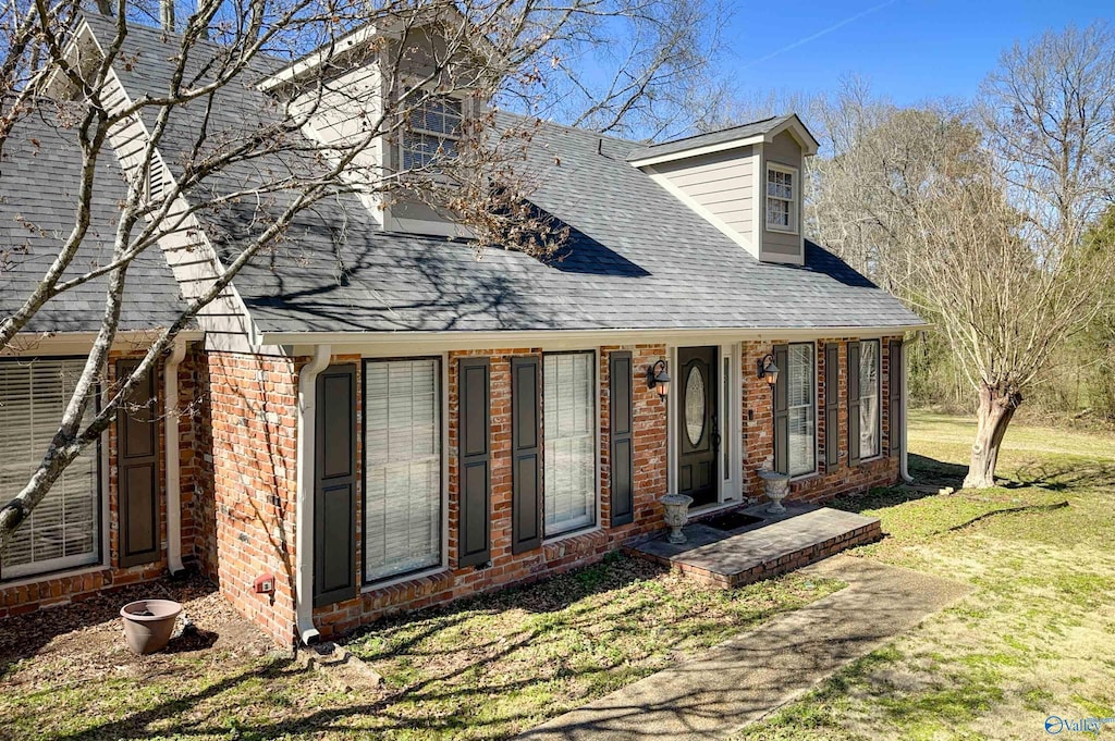 cape cod-style house featuring roof with shingles, a front lawn, and brick siding