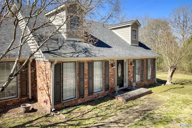 cape cod-style house featuring roof with shingles, a front lawn, and brick siding