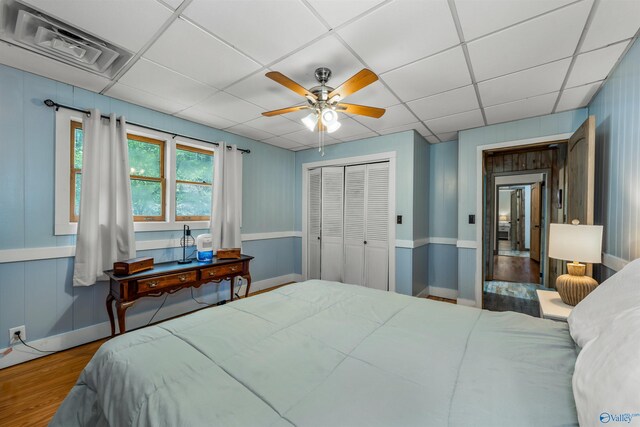 bedroom with wood-type flooring, a drop ceiling, ceiling fan, and a closet