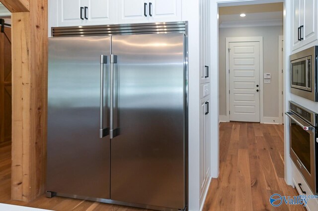 kitchen featuring built in appliances, recessed lighting, baseboards, white cabinets, and light wood-type flooring