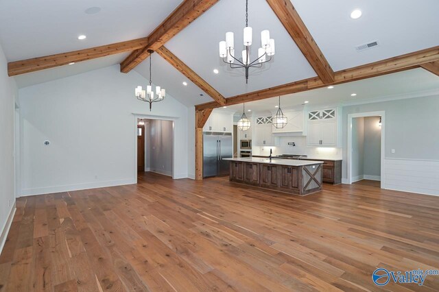 kitchen featuring wood-type flooring, stainless steel appliances, an island with sink, and backsplash