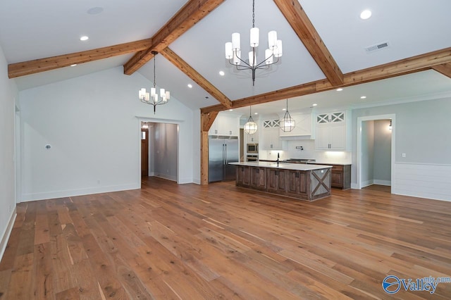 kitchen featuring a center island with sink, white cabinets, open floor plan, decorative light fixtures, and built in appliances