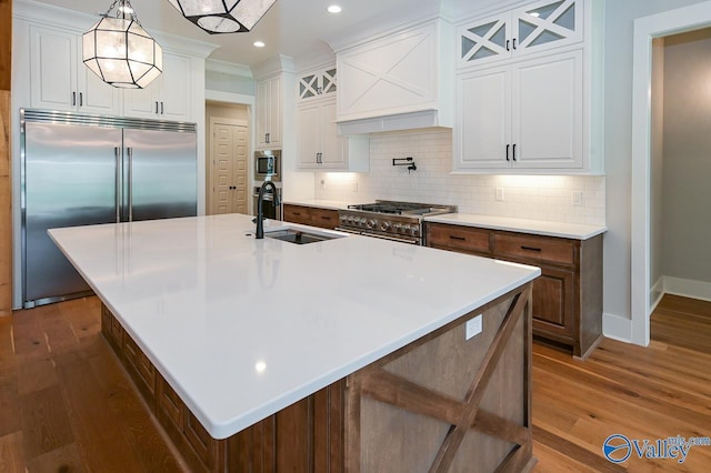 kitchen with white cabinetry, a sink, an island with sink, and built in appliances