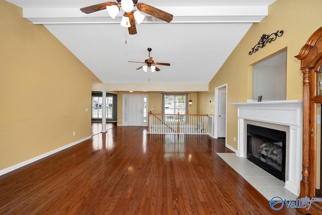 unfurnished living room with a ceiling fan, wood finished floors, vaulted ceiling with beams, and a healthy amount of sunlight