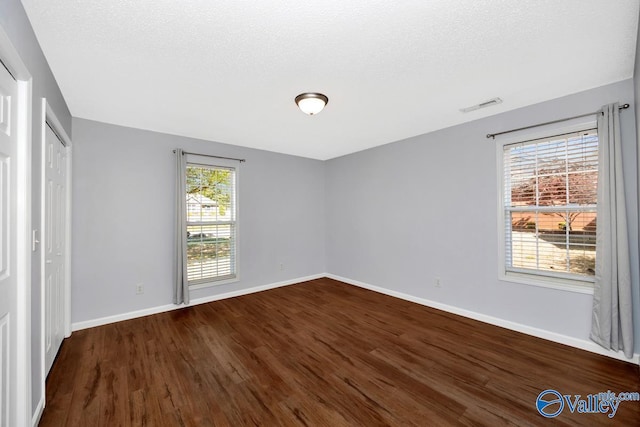 unfurnished bedroom with baseboards, dark wood-type flooring, visible vents, and a textured ceiling