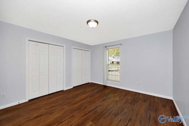unfurnished bedroom featuring baseboards, dark wood-style floors, and two closets