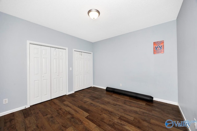 unfurnished bedroom with wood finished floors, multiple closets, and baseboards