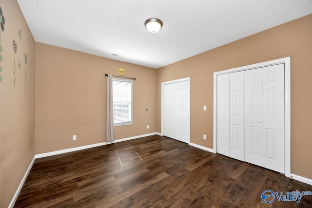 unfurnished bedroom featuring baseboards, two closets, and dark wood-style floors