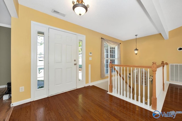 foyer entrance with wood finished floors, visible vents, baseboards, and beam ceiling