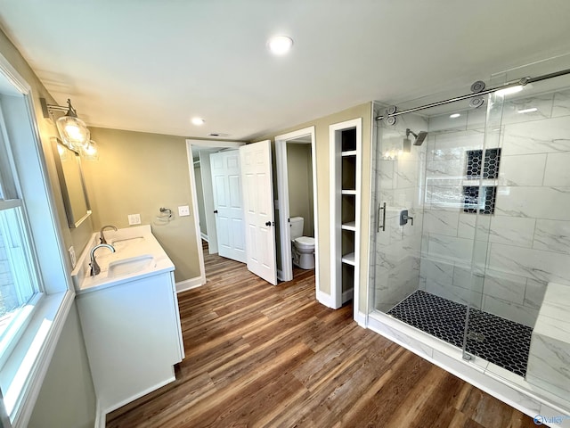 bathroom with toilet, a stall shower, vanity, wood finished floors, and baseboards