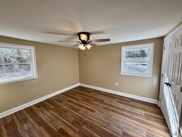 unfurnished bedroom featuring a closet, multiple windows, dark wood finished floors, and baseboards